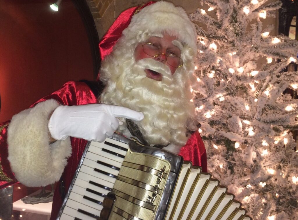 Kerstman met accordeon bij kerstboom